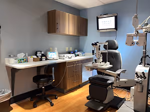 A room in an eye care clinic with a monitor, a chair, and an eye examination machine.