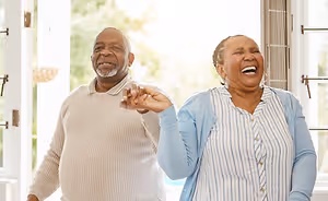 Two people are smiling and laughing in a room with a glass window