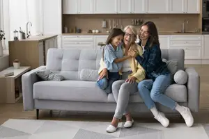 Three women and a young girl are sitting on a couch in the living room, smiling and posing for a photo.