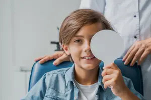 A young boy holding a mirror in front of his eyes at an eye doctor's office