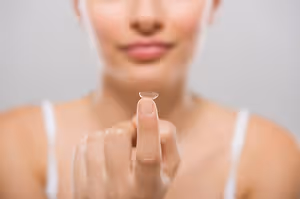 A woman is holding a contact lens in her hand.
