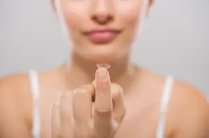 A woman is holding a contact lens in her hand.