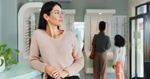 A woman with glasses is standing in front of a desk in an optical shop.