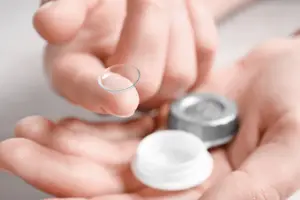 A hand holding a contact lens and a bottle of contact lens solution