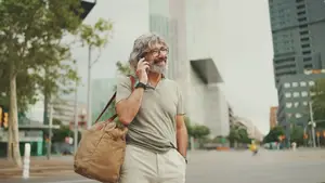 A man with gray hair wearing eyeglasses and a green t-shirt is walking on the road while talking on the phone.