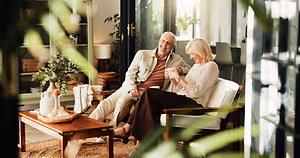 A man and woman are sitting on a couch and seem to be talking to each other in a room.