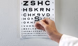 A hand is holding a piece of plastic that is covering a letter on a vision test chart, indicating a possible visual impairment assessment