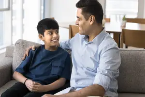 A smiling boy sitting next to a man on a couch with a plant in the background