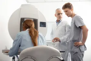 A medical professional is explaining something to a student and another medical professional in a room with medical equipment