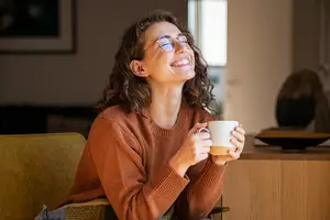 A woman sitting on a chair, smiling, and holding a coffee cup.
