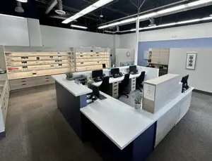 An office interior with desks, chairs, cabinets, a monitor, a picture frame, and lamps. 
