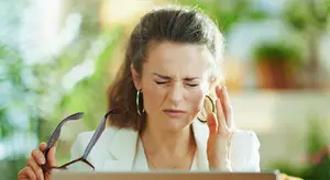 woman in white blazer crying while holding a pair of glasses