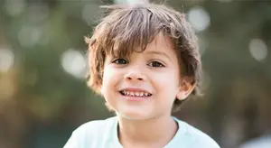 A smiling young boy with brown hair wearing a light blue shirt