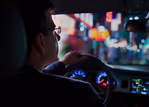 Man wearing glasses driving a car in a city at night