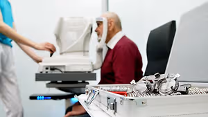 An elderly man is having an eye test at a clinic, with a healthcare worker nearby.
