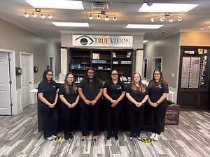 Six women dressed in black uniforms pose for a picture in a store with a sign that reads True Vision