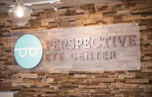 An image of a sign for Perspective Eye Center mounted to a brick wall with a warm lighting fixture overhead