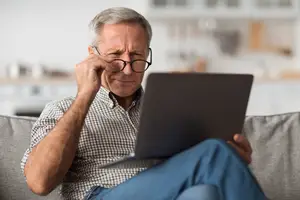 Older man sitting on a couch and working on his laptop computer.