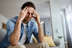 Man sitting on couch with his head in his hands looking distressed