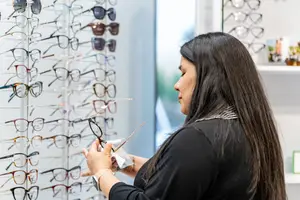 A woman holding a pair of glasses while looking at the display of other glasses inside the shop