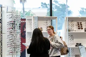 Two women standing in front of a glass display case with glasses in a store.