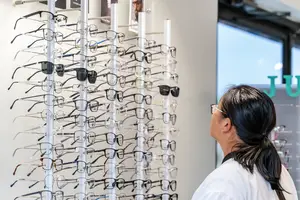 A woman wearing glasses is looking at a display of eyeglasses in a shop