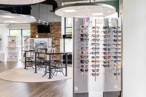 Indoor display of sunglasses on a stand with a table and stools nearby