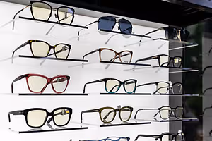 A collection of eyeglasses in different colors and styles are displayed on a white wall in a store.