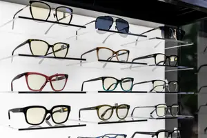 A collection of eyeglasses in different colors and styles are displayed on a white wall in a store.