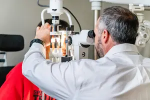 A man is checking the eye of a young person with an eye instrument.