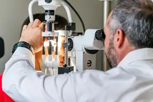 A man is examining a woman's eye with a ophthalmoscope in a hospital room.