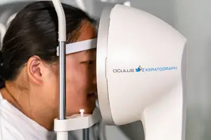 An Asian woman is having her eyes examined with an Oculus Keratograph eye scanning device.