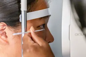 A woman is having an eye examination with a white headband on her head.