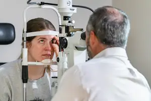 A woman is having her eyes examined by a doctor in a white lab coat.