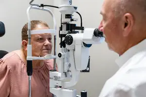 A woman is undergoing an eye examination with a man standing next to her using an ophthalmoscope