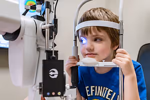 A young boy is sitting in a chair and examining his eyes with a device in an indoor setting