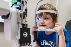 A young boy is sitting in a chair and examining his eyes with a device in an indoor setting