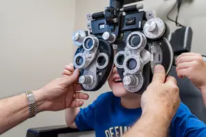A young boy is having an eye examination with an optometrist holding an ophthalmoscope to his eye.