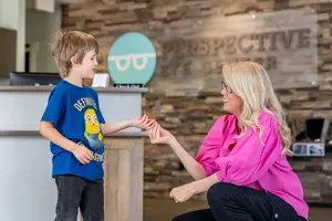 A woman and a boy are smiling and holding hands in front of a wall with a sign that reads Perspective Eye Center.