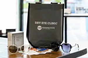 Dry Eye Clinic tote bag, a box of Eye Care Essentials, and two pairs of sunglasses on a wooden table