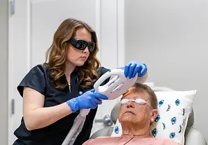 An elderly man is having his eyes treated by a woman in a medical office with a laser machine.
