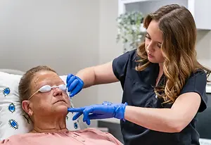 An older woman lying down on a hospital bed getting her eye examined by a doctor