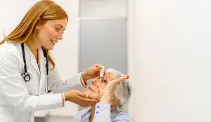 A doctor administering eye drops to an elderly woman in a medical setting.
