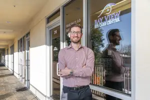 A man wearing glasses and a watch is standing outside of an office building.