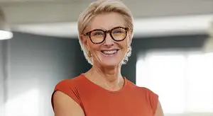 Portrait of a happy woman in an orange shirt with glasses smiling and standing in a room