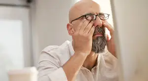 man looking at himself in a mirror rubbing his eyes with his hands