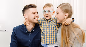 Three smiling people, a boy wearing glasses, a man, and a woman standing together