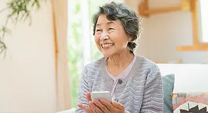 Happy older woman smiling and holding a mobile phone while sitting on a couch.