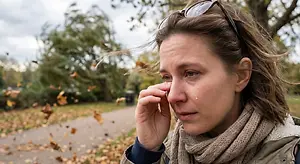 A woman is crying outdoors in a park with fallen leaves on the ground