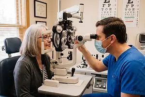 Optometrist examining a patient’s eyes with a slit lamp in an exam room.